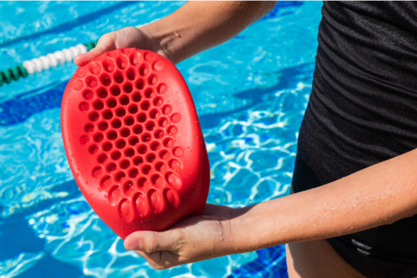 Someone is holding a Hammer Head Swim Cap inside out above a pool to display its honeycomb impact technology that keeps swimmers in the pool safe underwater