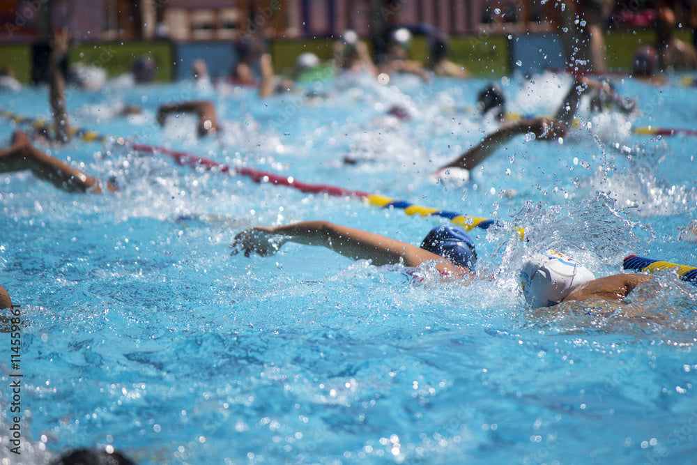Crowded swimming pool warm up lanes showing why swimmers need hydrodynamic swim cap and a swim cap with impact protection and extra comfort. Pool water is splashing in high traffic lanes. Athletes are swimming over other swimmers with risk of head injuries.