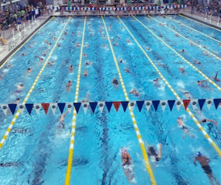 Swimming pool with multiple swimmers in lanes, surrounded by spectators.