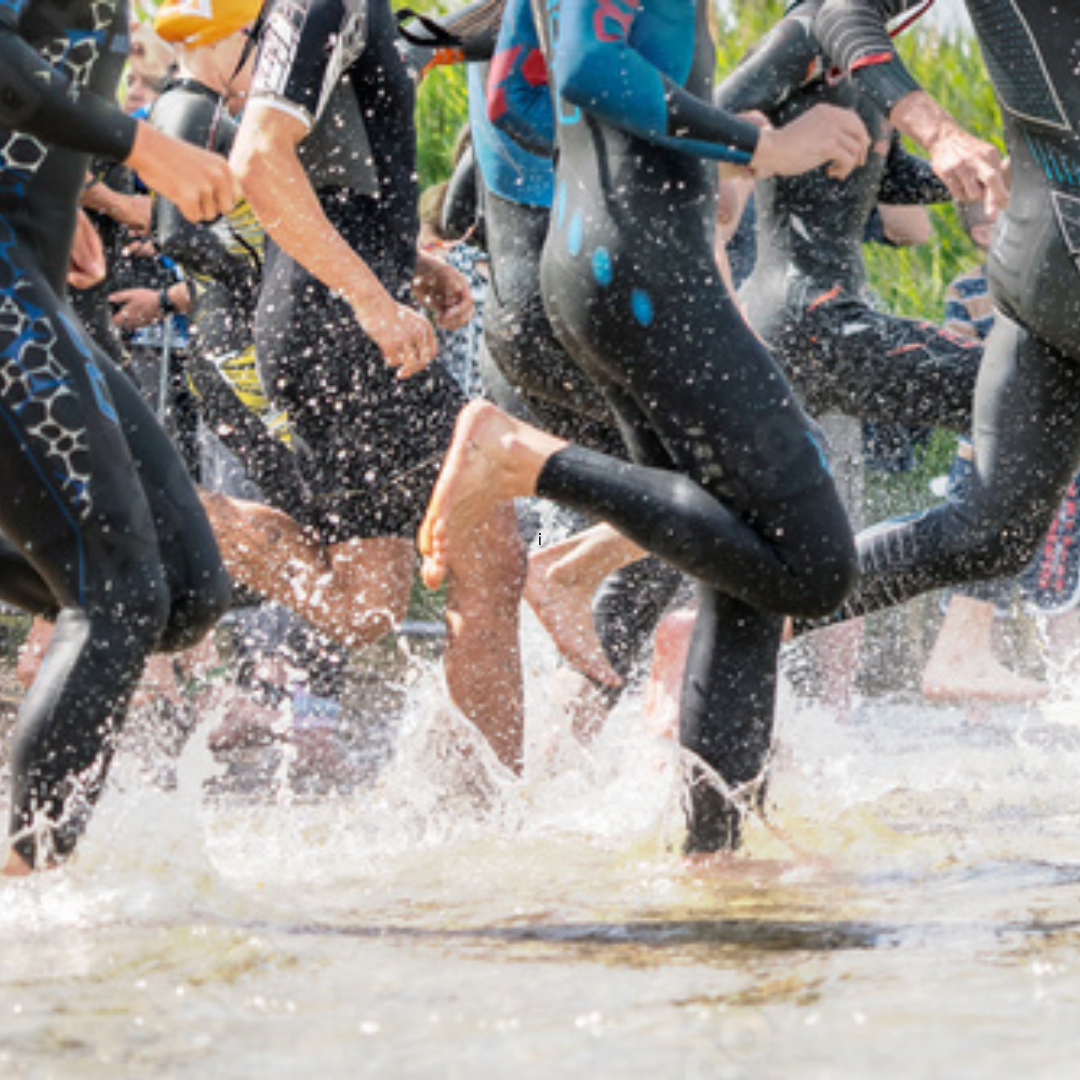 People in wetsuits running into the water in the mass swim start pf a triathlon open water swim event. As they get in deeper waters congestion and chaos can lead to head injuries. Hammer Head offers a seamless swim cap, a protective swim cap and durable swim cap for competitive triathletes. 